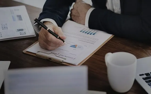 Profissional em mesa de escritório escreve em documento, ilustrando como fazer relatório contábil