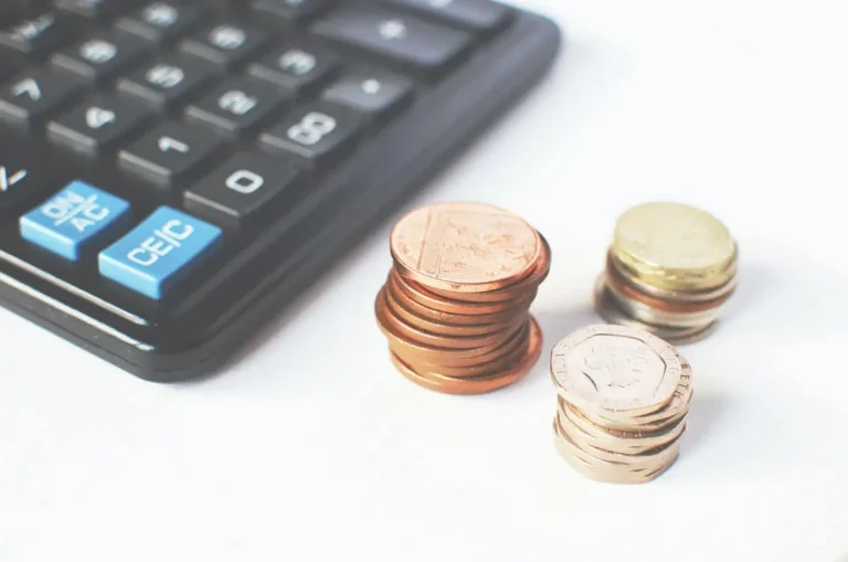 Calculadora e pilhas de moedas representando um fato contábil misto em registros financeiros