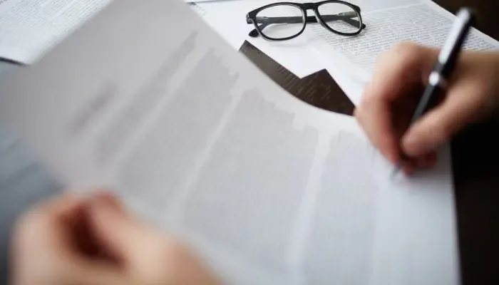 Imagem de mãos brancas com caneta escrevendo em papel ilustrando exemplos de editais.