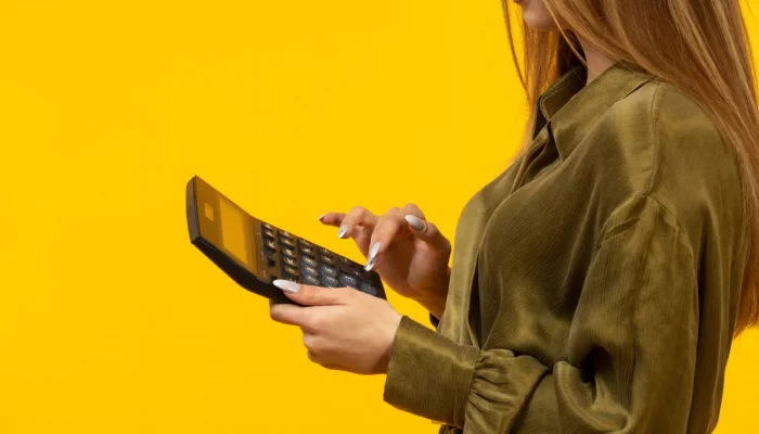 Uma mulher em um fundo amarelo mexendo na calculadora